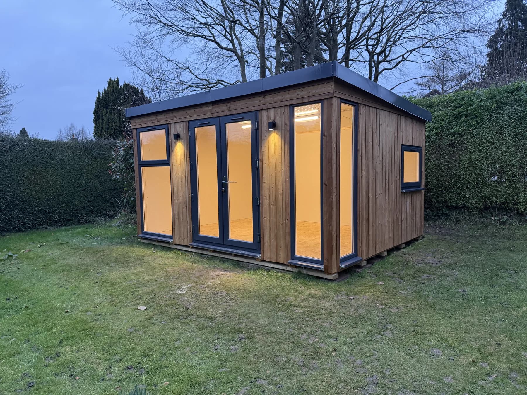 Dunster House garden room in Lower Kingswood with timber cladding and warm lighting at dusk