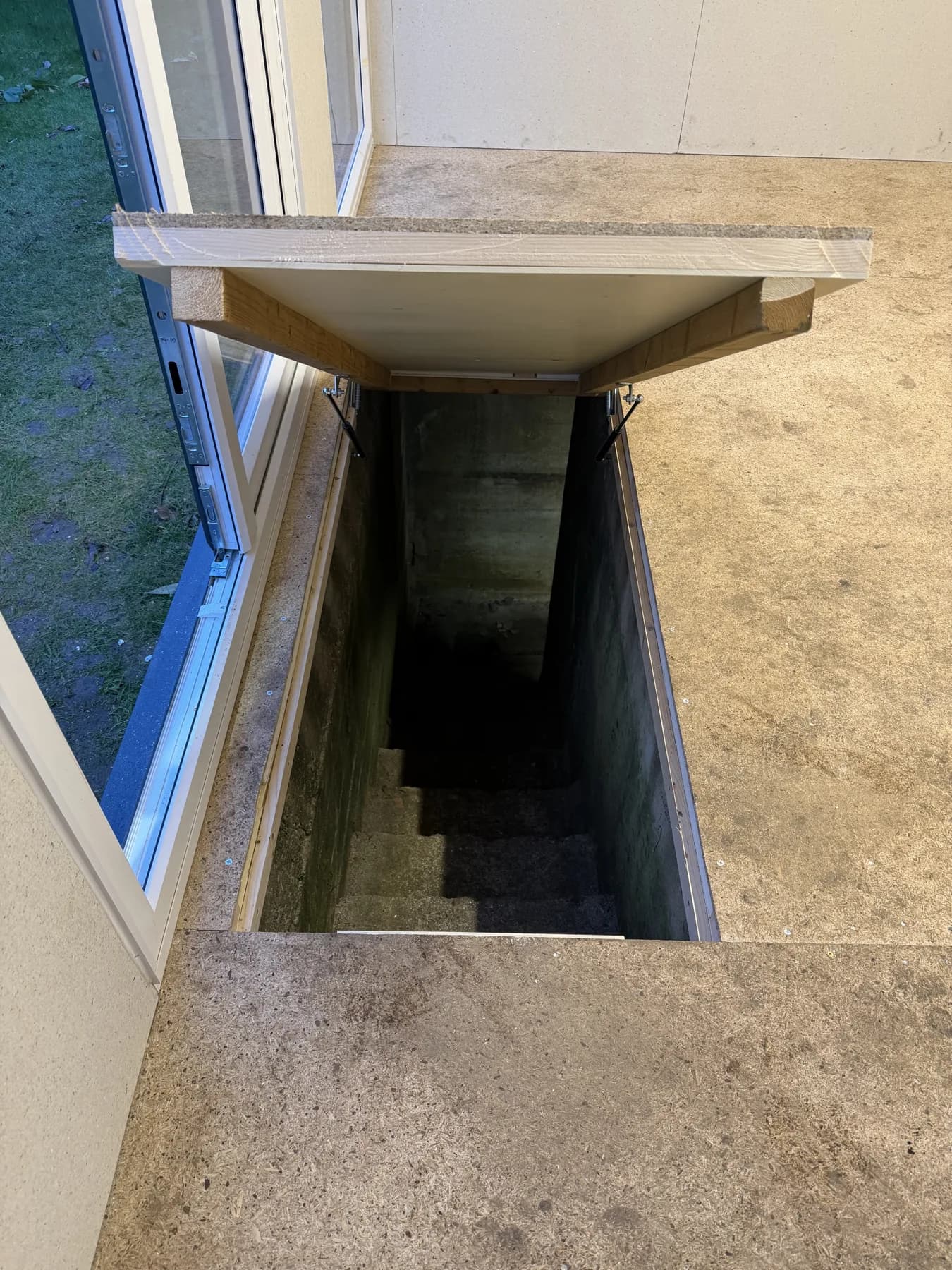 The open floor hatch preserves access to the old bunker beneath the garden room.
