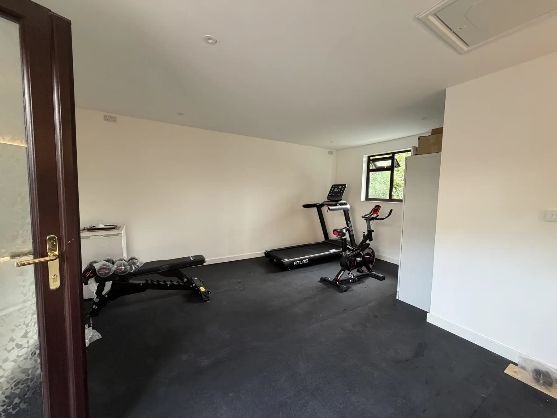 Purley garage conversion with gym equipment, white walls and dark flooring