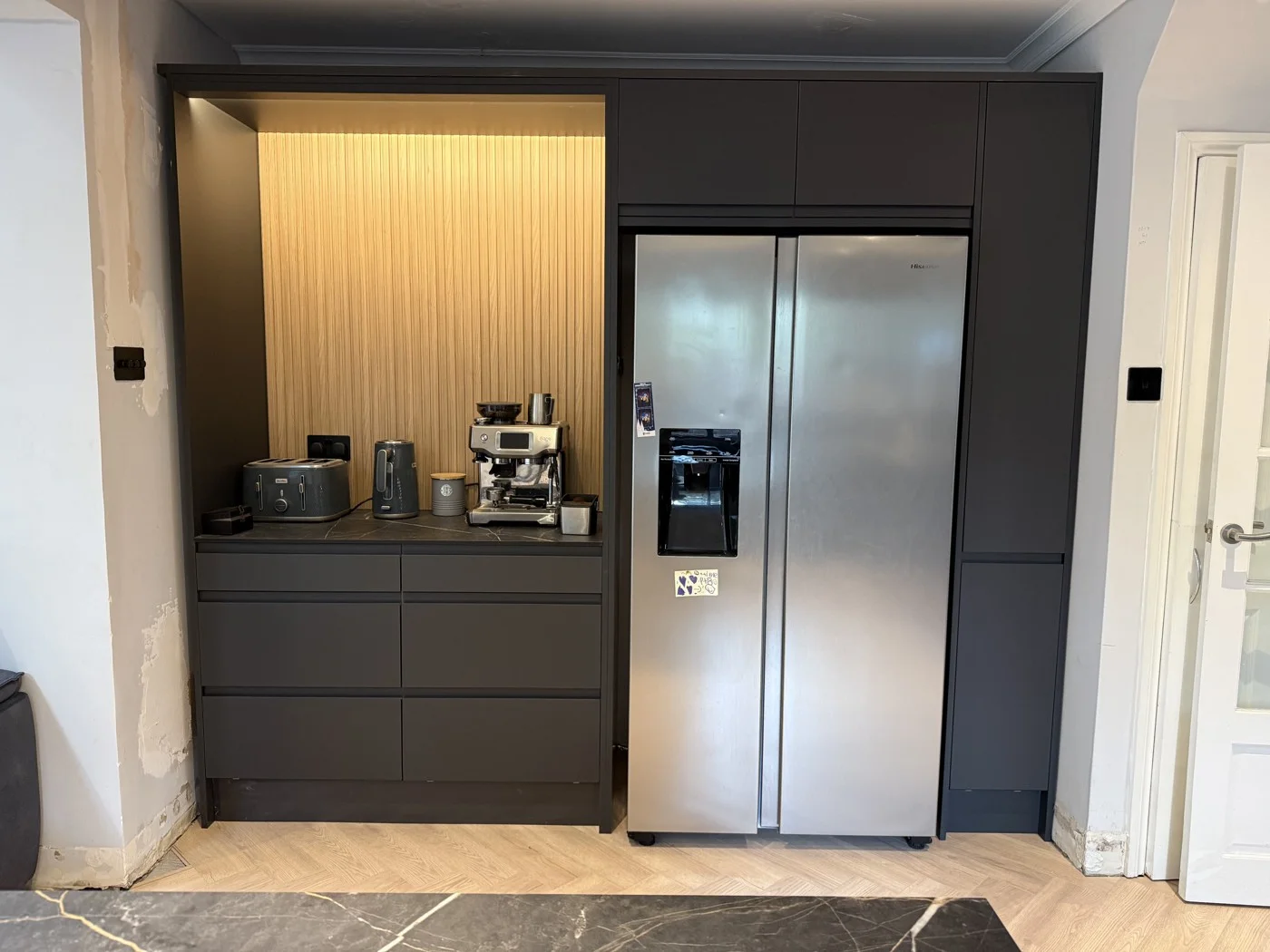 Cabinetry and illuminated coffee area beside the fridge.