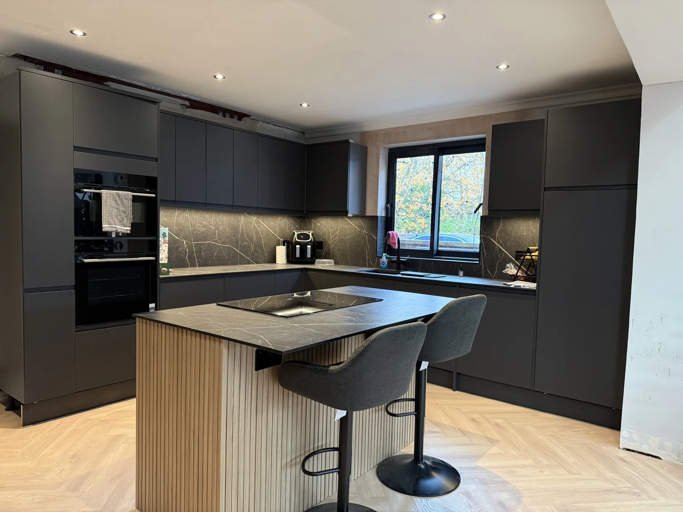 New kitchen with island, dark cabinetry and herringbone flooring.
